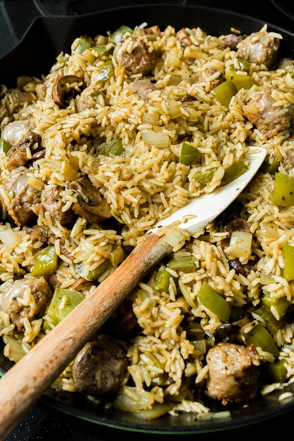 Cooked rice, sausage, and vegetables in a skillet on the stovetop with a silicone and wood spatula.